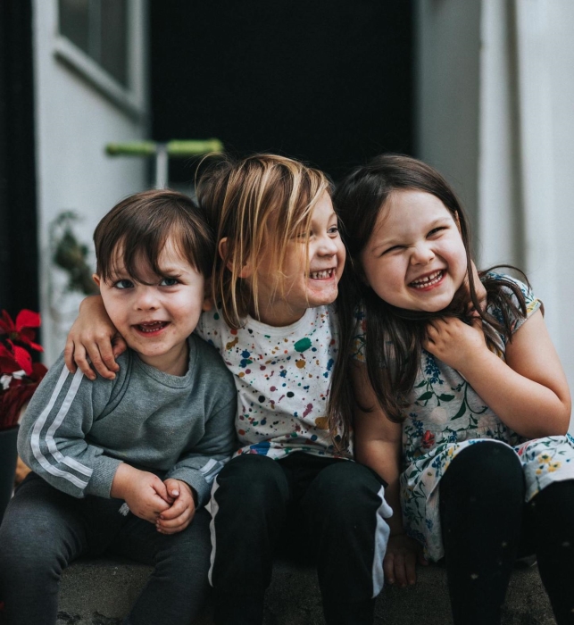 Three kids laughing and smiling sitting on the starcase in front of a house