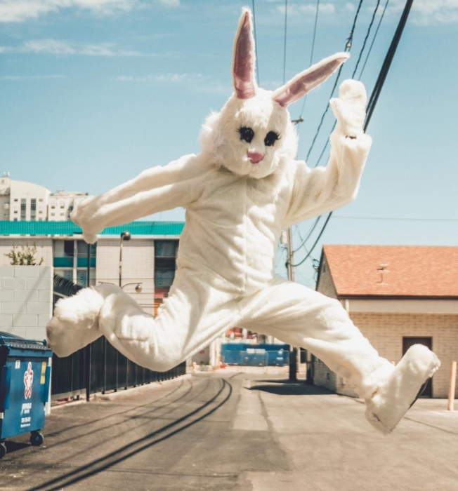 Person in a white bunny costume jumping through the streets in the city, on a sunny day