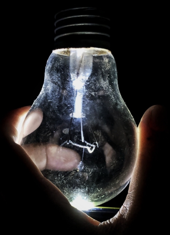 A hand holding up a lightbulb in the dark